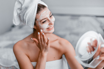Woman in her room making facial mask holding mirror in his hands. Morning skin care routine. Stay...