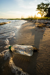 a plastic bottle full of water being recycled from a dirty beach during sunset