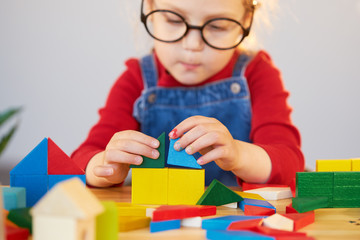 Online distance learning at home during quarantine. A smart child with glasses collects a multi-colored constructor at a table in a classroom.