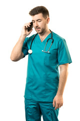 A young male surgeon with a beard in a blue suit is talking on the phone on a white background. Vertical frame