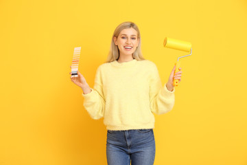 Young woman with color swatches and paint roller on yellow background