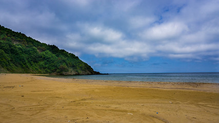 A deserted beach under sky with clouds. Abandoned island and greenery hill with  cloudy sky.