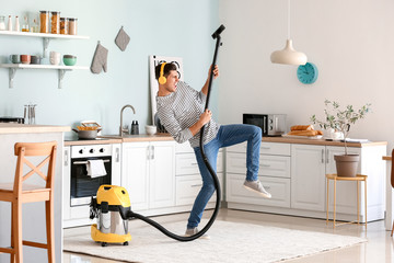 Young man listening to music while hoovering floor in kitchen