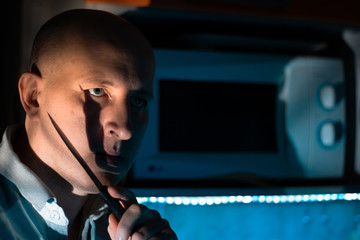 A bald man stands holding up a knife near a microwave in the kitchen at night. Domestic violence