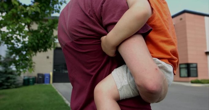 Father holding toddler son in arms as they watch firetrucks leave fire station - from behind