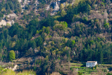 A wide angle shot of the green low Alps mountains and a lone building at the bottom of the mountain