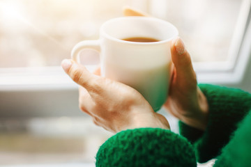 Cup close-up. Feminine and beautiful athletic young brunette woman is sitting on a wooden windowsill near the window. The female model is dressed in white underwear. Tenderness and calm concept