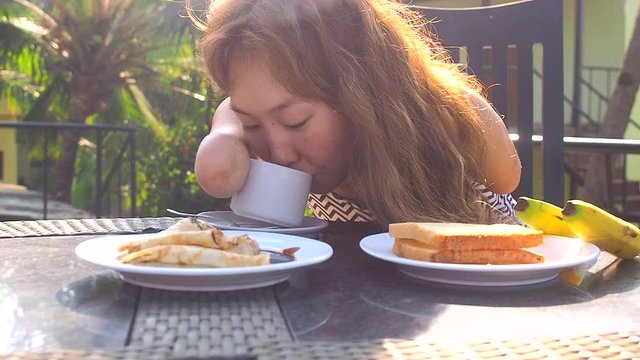 beautiful asian woman eating breakfast at tropical resort.she is drinks cup of tea or coffee