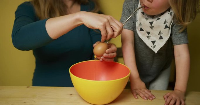 Little preschooler blowing out eggs with his mother for Easter decorations