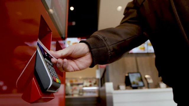 Buyer makes payment through a payment terminal with a credit card, enters a PIN code. Banking services of electronic money, making transaction. Man uses kiosk to order food at fastfood restaurant.