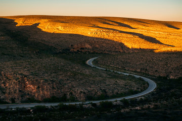 Fototapeta na wymiar A curved road through desert terrain at sunset