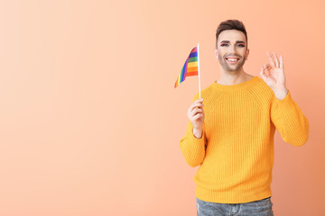 Portrait of young transgender woman with flag of LGBT showing OK gesture on color background