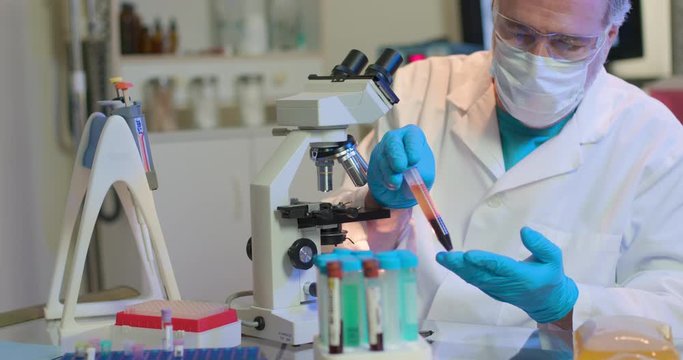 A medical researcher in a small laboratory holds a blood plasma sample he will use in trial tests for treating COVID19 patients.