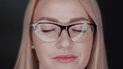 Fototapeta na wymiar close up portrait of a beautiful young blonde hair business woman with glasses who standing with closed eyes and then open them and confidently looks in camera. Slow motion front view video in 4K.
