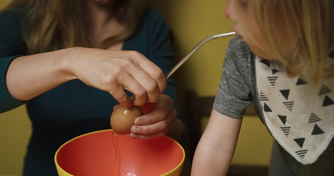Mother helping her preschooler blow an egg with a straw
