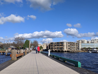 couple walking with arms linked together down the Lake Washington boardwalk on a bright, sunny day