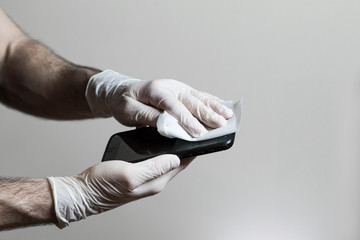 A mans hands wearing latex gloves wiping off his cell phone with a disinfecting wipe during the Covid 19 pandemic.