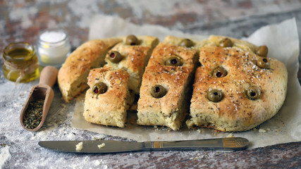 Selective focus. Macro. Fresh homemade focaccia with italian herbs. Cooking at home. Traditional italian bread with olives.