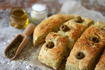 Selective focus. Macro. Fresh homemade focaccia with italian herbs. Cooking at home. Traditional italian bread with olives.