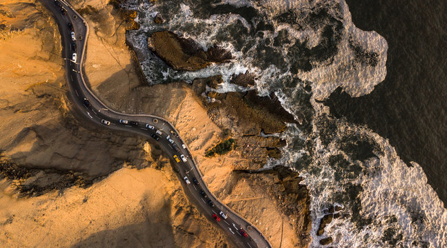 Aerial top-down view on the road at the cliffs next to the rocky coast with traffic during the sunset, Chorillos, Lima, Peru. 