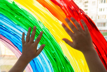 Close-up photo of child's hands touch painting rainbow on window. Family life background. Image of kids leisure at home, safety joy symbol. Chase the rainbow flashmob.