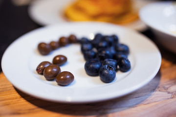 Berries and chocolate chip in a white plate with pancakes in the background.