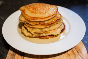 Fresh homemade classic pancakes with maple syrup in a white plate on a wooden board.