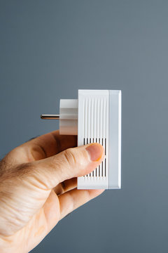 Man hand holding against light blue background a new powerline Ethernet internet adapter side view