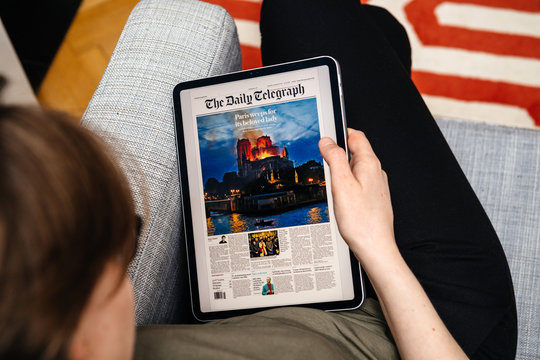 Paris, France - Apr 15, 2019: Woman Reading The Daily Telegraph On IPad Pro Apple News Plus Digital Newspaper Featuring Breaking News On Cover French Notre-Dame Cathedral On Fire Causing Damages