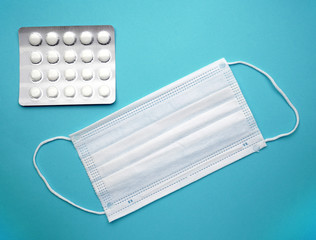 Disposable surgical face mask covers the mouth and nose and tablets on an isolated blue background.