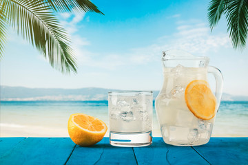 Cold, freshly made lemonade with ice on a wooden table under the palm trees on a tropical beach. Healthy, organic, detoxifying, vegetarian and vegan drinks. Space for text.