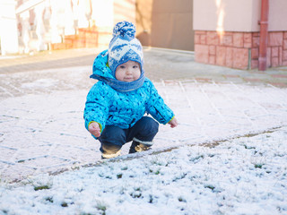A boy is playing in the snow. 0-1 child, a boy playing with snow on snowy ground. walking in a snowy park enjoying the first snow
