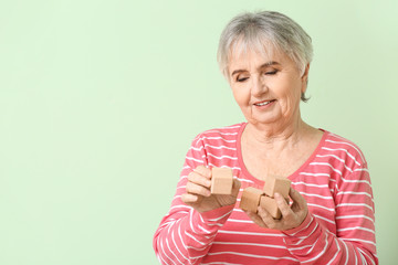 Elderly woman suffering from mental disability with cubes on color background