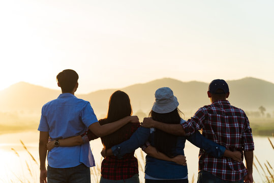 Group of happy friends are having fun with raised arms together in front of mountain and enjoy sunrise sunset showing unity and teamwork. Friendship happiness leisure partnership team concept.