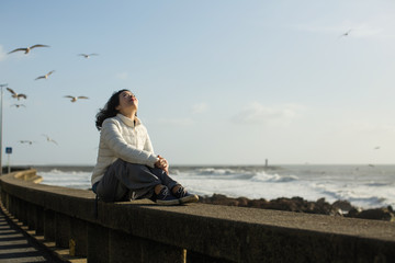 Beautiful mixed-race woman sits on the waterfront during the surf and gulls around.