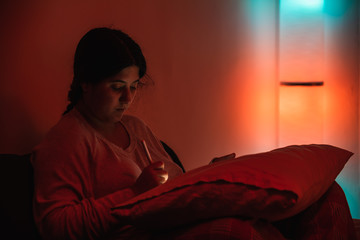 Young woman taking notes on a pro tablet with a digital pencil on a living room with connected color bulbs and a lamp with 3 of them at her side. The lights give a comfortable teal and orange ambient.