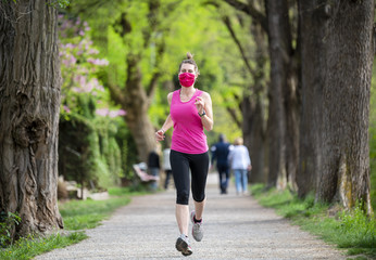 Stay in fit during quarantine. A sportive young woman is jogging outdoor, she have pink protective...