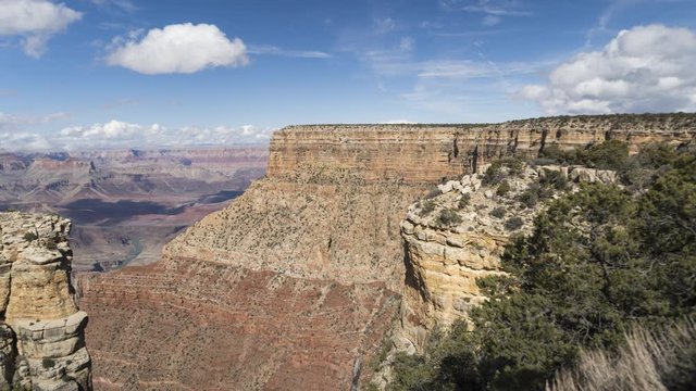 A wide motion timelapse shot of the Grand Canyon. The camera tracks right and tilts down to show the canyon below before tilting up to reveal clouds flowing over Moran Point.