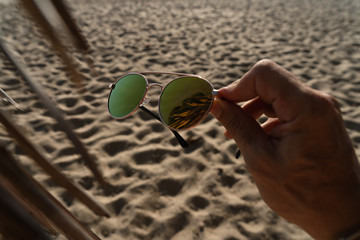 Man hand with sunglasses on a background of palm leaves and sand on the beach