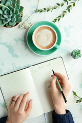Cup of coffee on table of woman writing in notebook