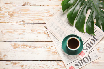 Fototapeta na wymiar Cup of coffee, newspaper and tropical leaf on light wooden background