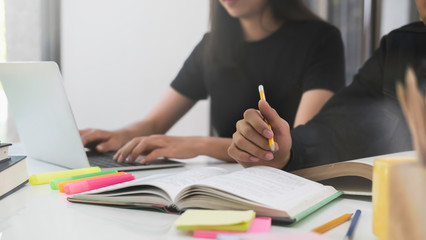 High school or college using laptop while sitting at table. Group students studying and reading with books in library. Students helps friend catching up and learning tutoring. education concepts