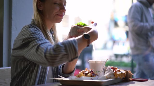 Happy hipster girl enjoying cheat meal day for eating unhealthy food after diet lifestyle, Caucasian woman checking received email on modern smartphone during lunch in bistro cafeteria
