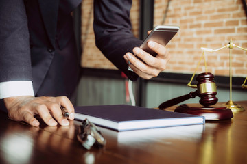 Justice and law concept. Gavel on sounding block in hand's Male judge at a courtroom, working with smart phone, report the case on table in modern office.