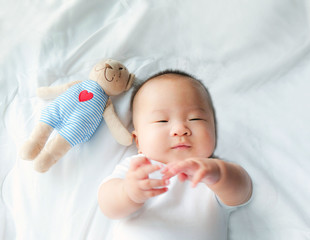 Portrait of a newborn Asian baby boy on the bed , Charming Fat baby 5 month old lies in bed and the doll ,enjoy and happy,soft and selective focus