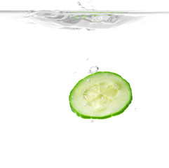 Falling of fresh cucumber slice into water against white background