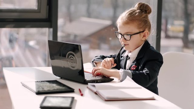 Primary school girl is on distance learning at home. The pupil is working with a laptop and taking notes on her e-classes. The child continues her studying during quarantine.