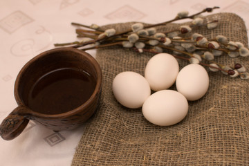 Willow twigs and white eggs on the table next to an earthenware mug