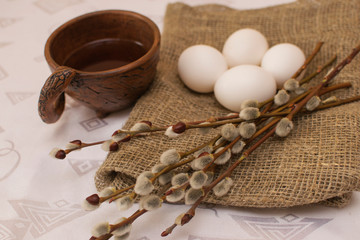 Willow twigs and white eggs on the table next to an earthenware mug