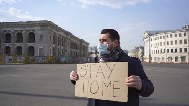 Pandemic team. Man in medical mask stand with poster on city empty street. 